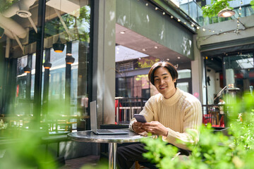 Wall Mural - Young confident Japanese businessman using mobile phone, looking camera