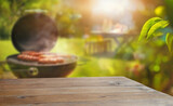 Fototapeta Perspektywa 3d - summer time in backyard garden with grill BBQ, wooden table, blurred background