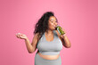 © Prostock-studio - Positive black plus size woman in sportswear holding jar of fresh smoothie, standing on pink studio background