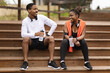 © Prostock-studio - Cheerful young black couple sitting on stairs, talking, relaxing with bottles of water in summer