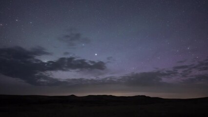 Wall Mural - nighttime lapse of a star filled sky with clouds moving from left to right and weak aurora. the dist
