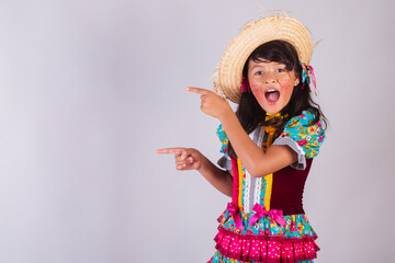 Child, Brazilian girl, with June party clothes, presenting something on the side, product, advertisement.