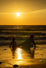 Two Children Sitting On The Beach By Sunset