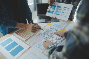 Close up ux developer and ui designer brainstorming about mobile app interface wireframe design on table with customer breif and color code at modern office.Creative digital development agency