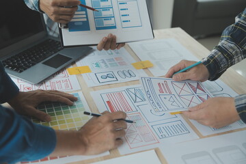 Close up ux developer and ui designer brainstorming about mobile app interface wireframe design on table with customer breif and color code at modern office.Creative digital development agency
