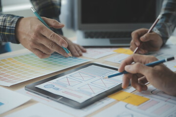 Close up ux developer and ui designer brainstorming about mobile app interface wireframe design on table with customer breif and color code at modern office.Creative digital development agency