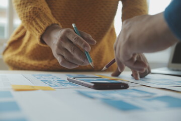 Close up ux developer and ui designer brainstorming about mobile app interface wireframe design on table with customer breif and color code at modern office.Creative digital development agency