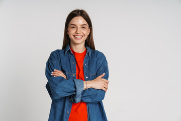 Wall Mural - Smiling woman standing with arms folded isolated over white wall