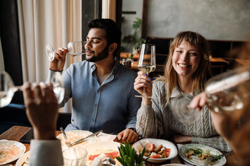 Group of young friends talking and drinking wine while dining in restaurant