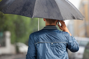 Wall Mural - Man talking on cell phone under umbrella in rain