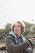 Man listening to headphones against chain link fence