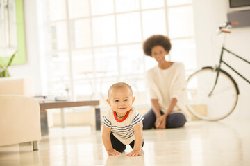 Wall Mural - Mother watching baby boy crawl on living room floor