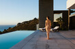 © KOTO - Woman in dress walking along infinity pool overlooking ocean