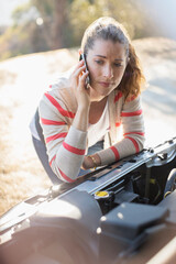 Wall Mural - Frustrated woman talking on cell phone and looking at car engine