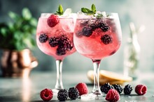Two Tall Gin Glasses With Pink Gin And Wild Berry Tonic Served On Ice, Decorated With Frozen Berries And Mint Leafs