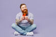 © ViDi Studio - Full body young redhead bearded man he wearing violet t-shirt casual clothes hold in hand use mobile cell phone in blue case isolated on plain pastel light purple background studio. Lifestyle concept.