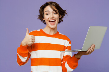 Wall Mural - Young smiling happy fun caucasian woman wearing casual clothes sweatshirt hold use work on laptop pc computer show thumb up isolated on plain pastel light purple background studio. Lifestyle concept.