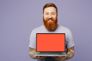 Young redhead bearded IT man wear violet t-shirt casual clothes hold use work on laptop pc computer with blank screen workspace area isolated on plain pastel light purple background studio portrait.