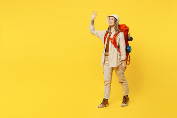 Full body happy young woman carry bag with stuff mat waving hand greet meet isolated on plain yellow background. Tourist leads active lifestyle walk on spare time Hiking trek rest travel trip concept