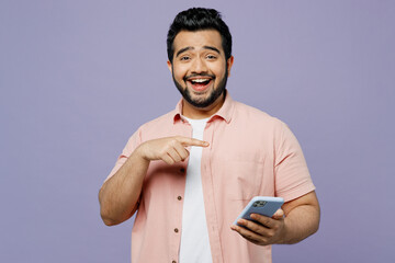 Wall Mural - Young Indian man he wearing pink shirt white t-shirt casual clothes hold in hand use point index finger on mobile cell phone isolated on plain pastel light purple background studio. Lifestyle concept.
