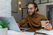 © zinkevych - Young bearded man freelancer in glasses working at home or in cafe with laptop.