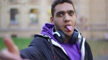 Selfie POV Of Joyful Young African American Man Sticking Tongue Out Making Faces In Slow Motion. Portrait Of Cheerful Carefree University Student Having Fun Looking At Camera Grimacing
