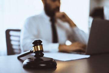 Wall Mural - Focus wooden gavel hammer on blur background of lawyer working with legal document on desk at law firm office. Lawful hammer for righteous and equality judgment by lawmaker and attorney. Equilibrium