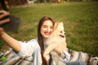 © Bogdan - Caucasian girl student female pet owner taking selfie photo with dog, image on smart phone, having video call conversation with dog online in park