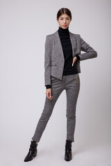 Wall Mural - Fashion photo of a beautiful elegant young asian woman in a pretty gray suit, pants, trousers, jacket, blazer, black top posing over white, soft gray background. Studio Shot, portrait. Slim figure