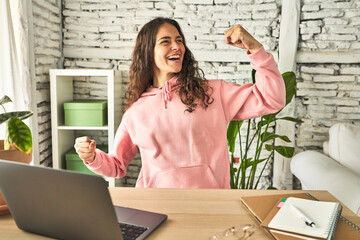 Young student woman studying in her home raising fist after a victory, winner concept.