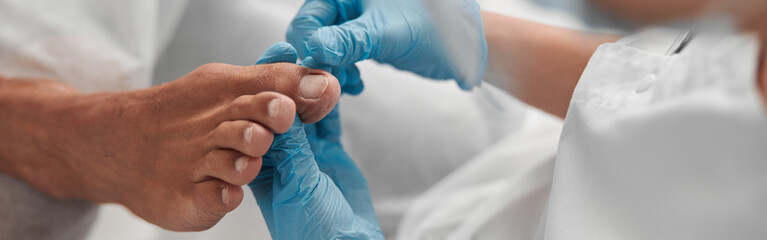 Beautician in gloves examines toenail of man client before pedicure procedure in salon