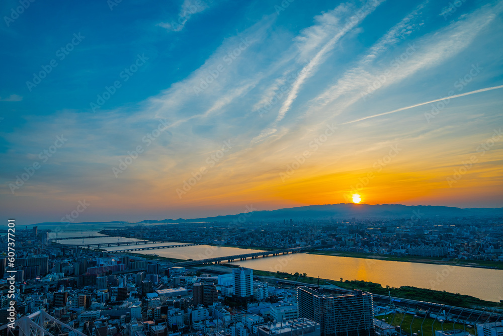夕焼け空、綺麗な夕陽が沈もうとする都会、そして川の水面に映る