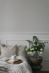 Wall Mural - Breakfast in bed. Cup of coffee, wicker tray. Bouquet of white viburnum, fern and solomons seal flowers. Modern boho night stand. Bedroom view. Beige pillows, blanket. Blurred background, vertical.