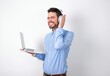 © Roquillo - Happy businessman wearing blue t-shirt with headphones over white background ignores loud music and plugs ears with fingers asks to turn off sound