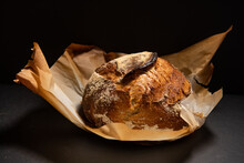 Fresh Sourdough Bread Loaf In Browned Parchment Paper Against A Black Background