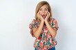 © Jihan - Stupefied beautiful teen girl wearing flowered dress over white studio background expresses excitement and thrill, keeps jaw dropped, hands on cheeks, has eyes popped out