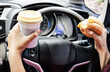 forbidden and perilous with close-up of woman's hand, holding burger and coffee, engaged in reckless eating and drinking While driving car