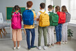 © Studio Romantic - Back to school concept. Group of school children with backpacks. Backside view from behind six students with colorful pink, blue, yellow, green, red and grey bags standing together in the classroom