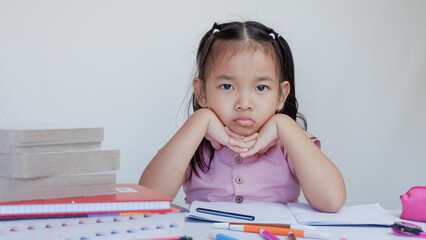 annoyed schoolgirl writes homework leaning against her hand.