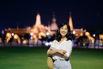 Portrait young beautiful asian woman smiling while travel at Temple of the Emerald Buddha or Wat Phra Kaew in night view point, Bangkok, Thailand.