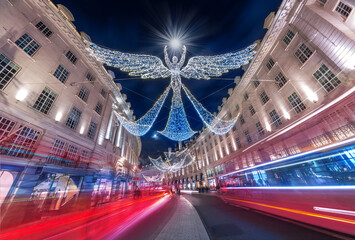 Wall Mural - Beautiful Christmas scene outdoors on the Regents Street with abstract angel shape decorated by lights and red double decker bus in motion, in London, UK