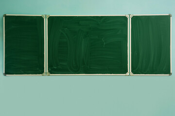 Long empty green colored school chalkboard mounted on wall in classroom. Education and learning concept.