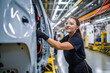 © InputUX - Confident female worker skillfully operating high-tech machinery in a modern automotive manufacturing setting, candid shot, generative ai