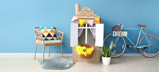 Poster - Child's playroom with toy cardboard house and bicycle near blue wall