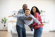 © sofiko14 - Active african american adults holding happy boy in arms together while testing imaginary flight at home. Energetic kid in jeans wear experiencing feeling of freedom and well-being thanks to parents.