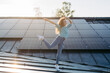 © Halfpoint - Portrait of young excited woman on roof with solar panels.