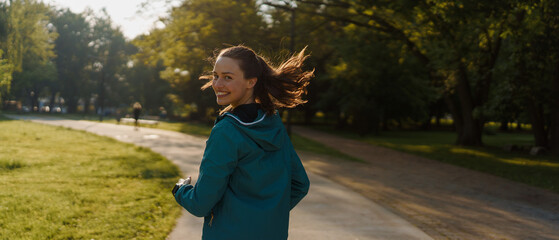 portrait of smilling young woman running in the city park in the early morning.