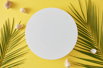 Wall Mural - Concept of beach vacation. Top view flat lay of seashells, palm leaves on yellow background with blank circle for advert or text