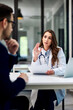 © bnenin - A female doctor holding papers and talking with a male patient with glasses on.