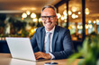 © Starmarpro - Smiling mid aged businessman ceo wearing suit sitting in office using laptop. Mature businessman professional executive. High quality photo Generative AI